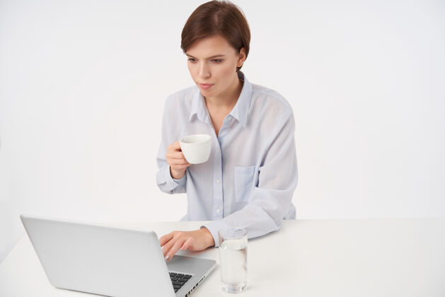 员工年轻漂亮的短发黑发女人的室内肖像 随意的发型 手放在笔记本电脑的键盘上 凝望着屏幕 一脸专注 与世隔绝工作长大休闲
