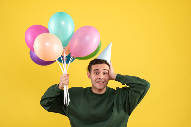 气球正面图穿着绿色毛衣的年轻人拿着气球站在黄色的地板上举行男人年轻人