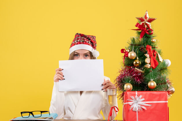 礼物前视图女医生坐在圣诞礼物持有黄色背景文件抱着快乐圣诞节