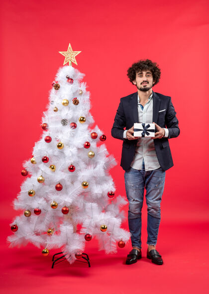 庆祝新年庆祝与严肃的年轻人手持礼物附近装饰白色圣诞树上的红色镜头镜头圣诞年轻人
