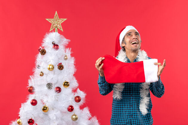 年轻人情绪激动的年轻人戴着圣诞老人的帽子 穿着蓝色的衬衫 手里拿着圣诞袜子 往上看帽子礼物年轻人