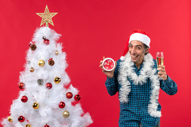 圣诞树带着圣诞老人帽子 举着一杯酒 抱着一个快乐的情绪化的年轻人圣诞钟杯子