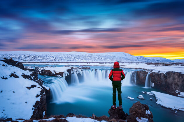 惊人冰岛冬天日落时的戈达福斯瀑布穿红色夹克的家伙看着戈达福斯瀑布水景观自然