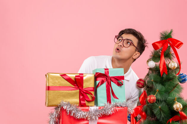 成人圣诞礼物和粉红色墙上的圣诞树周围的年轻人的正面视图圣诞树男性快乐