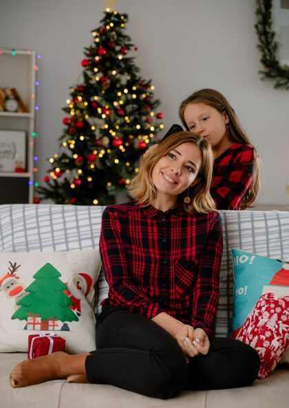 妈妈女儿坐在沙发上梳着妈妈微笑的头发 在家里享受圣诞节时光沙发享受圣诞节
