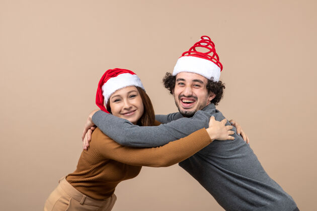 圣诞老人新年气氛和派对概念-年轻兴奋可爱的夫妇戴着圣诞老人的帽子拥抱对方灰色的镜头孩子帽子镜头