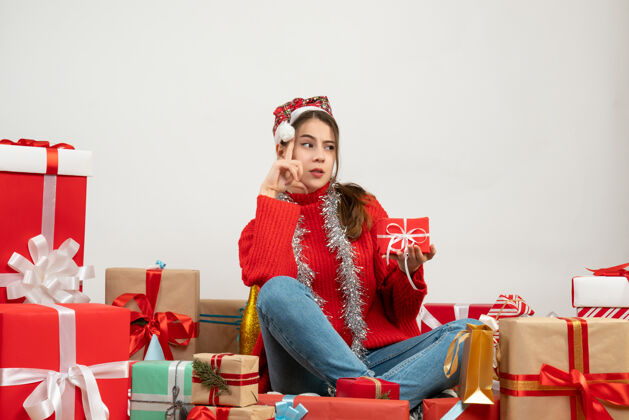 坐着戴着圣诞帽拿着礼物围坐在白色的礼物上思考的派对女孩圣诞老人抱着快乐