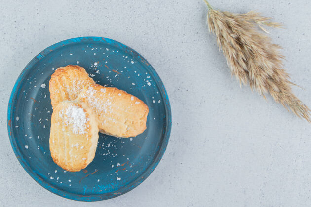 美味蓝色盘子上的片状饼干 旁边是大理石背景上的一根羽毛草香料茎羽毛草