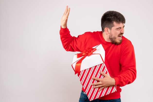 男性身穿红衫的年轻人在白色墙上的盒子里拿着圣诞礼物盒子成功人
