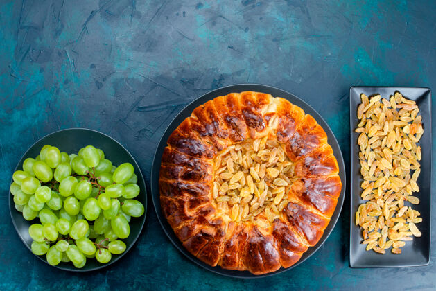 面团俯瞰图美味的烤蛋糕与葡萄干和新鲜的绿色葡萄深蓝色地板蛋糕馅饼糖甜饼干面团蔬菜蛋糕晚餐