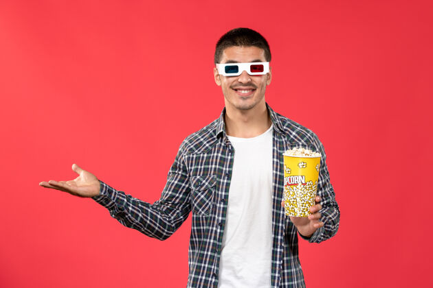 爆米花正面图戴着d墨镜的年轻男性手持爆米花包 微笑着站在浅红色的墙上看男性电影浅红色成人电影