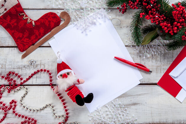 礼物纸上的空白纸上有一支钢笔和圣诞装饰品礼物 圣诞老人 桌子 花圈 庆典 信件 信封 钢笔 礼物 帽子 书写 信息 木制 传统 乡村 书写 降临 床单 装饰 空白 乡村 愿望 空