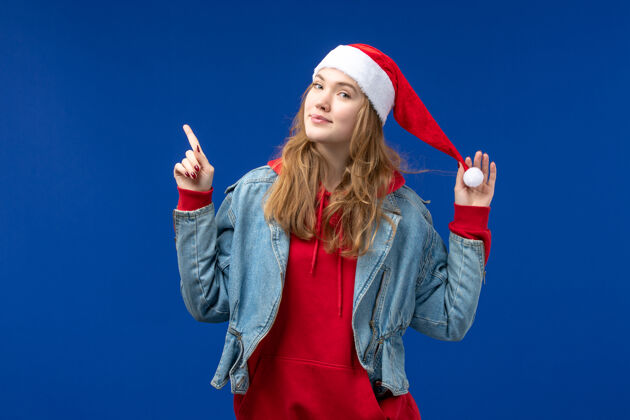 圣诞节正面图蓝色背景上戴着红帽子微笑的年轻女性新年假期圣诞节时尚快乐蓝色