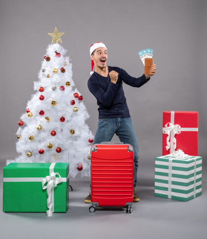 包在灰色的圣诞树旁 拿着旅行票的人欣喜若狂礼物圣诞老人礼物