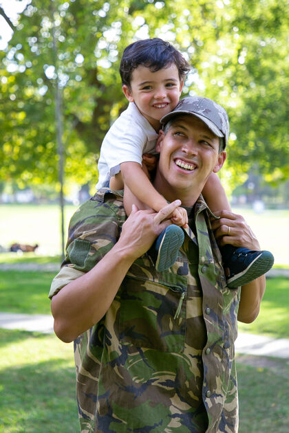 孩子高加索爸爸抱着儿子的脖子 微笑着快乐可爱的男孩抱着穿着军装的爸爸可爱的孩子和爸爸在城市公园散步家庭团聚 做父亲和回家的概念可爱公园回归