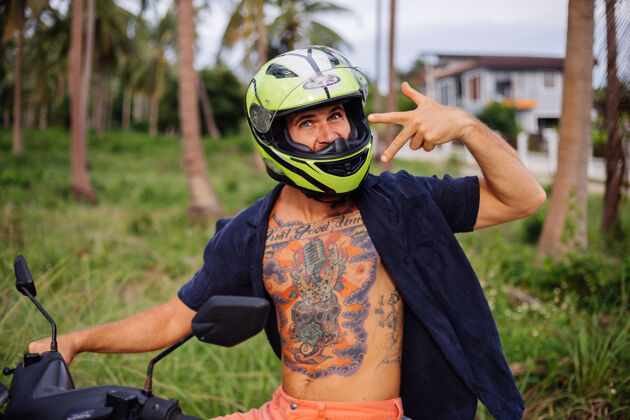 手在热带丛林的田野上纹着红色摩托车的壮汉运动自然人