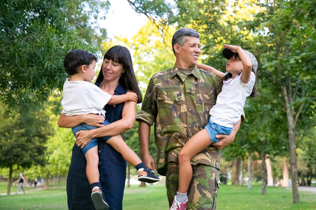 草快乐的军人带着妻子和孩子们在公园散步 教女儿做军礼手势全长 后视图家庭团聚或军人父亲的概念镜头回归力量