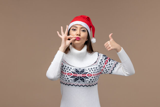 摆姿势正面图棕色背景上戴着红色圣诞帽的年轻女子圣诞感慨新年情感年轻成人