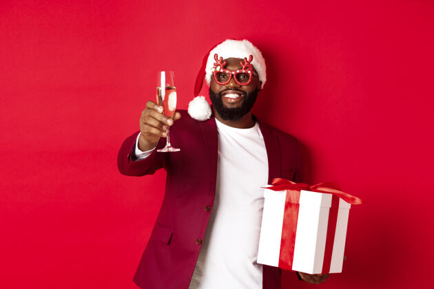 肖像圣诞节戴着派对眼镜和圣诞帽的英俊的非洲裔美国人年轻饮酒礼物