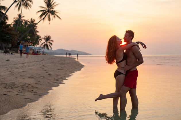 微笑年轻性感浪漫的情侣在夕阳下相爱 在夏日的沙滩上快乐地穿着泳衣一起玩幸福女性在一起