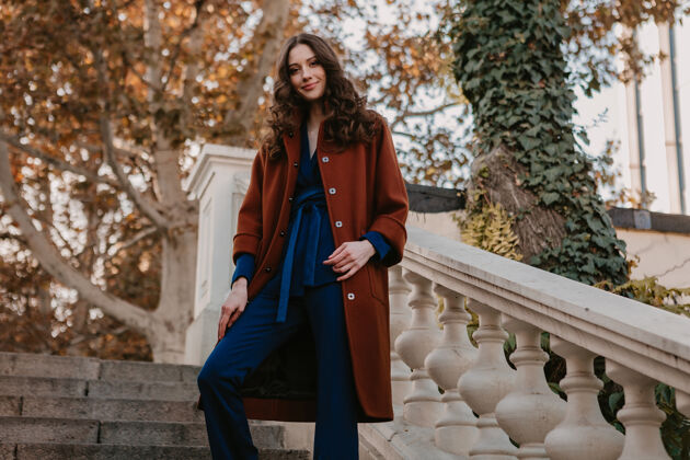 女士美丽时尚的微笑瘦身女子卷发走在街头楼梯上穿着温暖的棕色外套和蓝色西装 秋季时尚街头风时尚优雅年轻