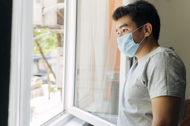 距离大流行期间 戴着医用口罩的男子从窗户往家里看的侧视图隔离口罩空间