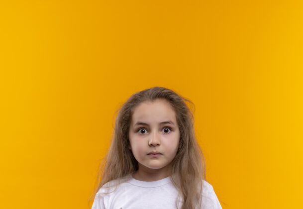 T恤惊讶的小女孩穿着白色t恤在孤立的橙色背景小学校女孩