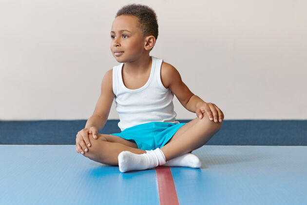 儿童可爱的非洲小运动员坐在垫子上双腿交叉放松后 集中训练体操身体健身