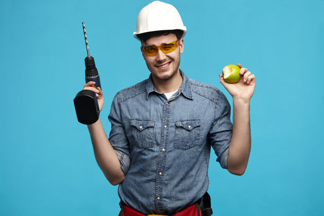 男性工作室照片勤劳英俊的年轻勤杂工戴着安全帽和眼镜摆姿势专业操练休闲