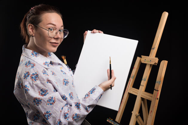 女性女艺术家在黑色背景上用画笔展示她的画布人工艺绘画