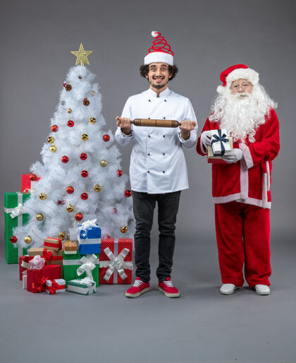 快乐圣诞老人和男厨师在灰色墙上围着圣诞礼物的正视图十二月圣诞老人厨师