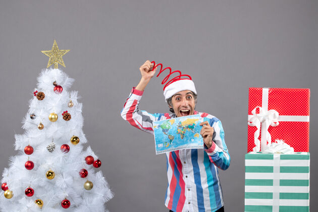 圣诞树前视图笑脸男子与螺旋弹簧圣诞帽举行世界地图帽子男人春天