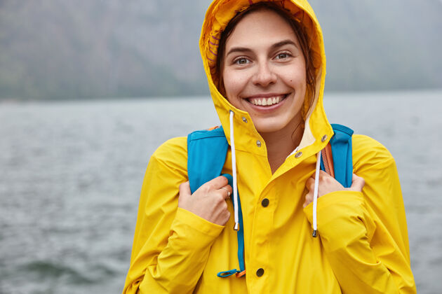 背包乐观的欧洲女人的剪短形象戴着黄帽 背着背包 有着灿烂的笑容白天湖泊外套