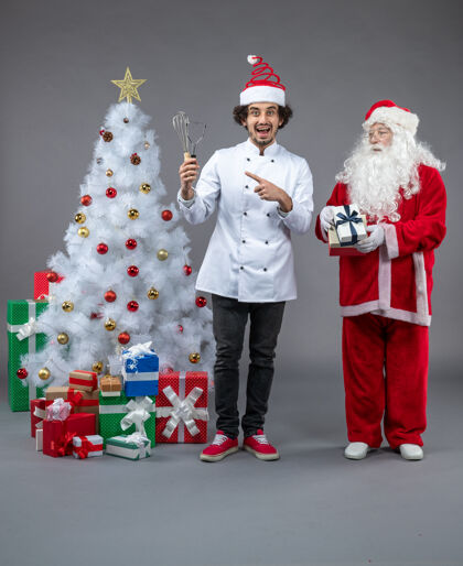 圣诞老人圣诞老人和男厨师在灰色墙上围着圣诞礼物的正视图圣诞老人人人们