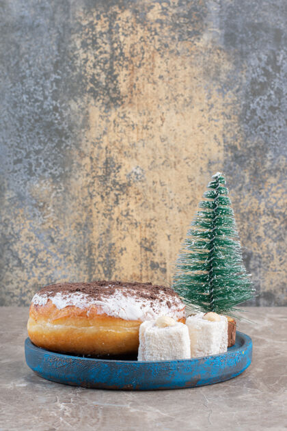 烘焙食品在大理石上的蓝色盘子上摆着花絮 甜甜圈和树雕像圣诞树Lokum美味