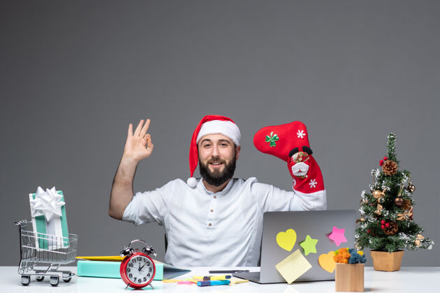 手圣诞节心情与年轻人戴着圣诞老人的帽子 穿上圣诞袜子 在白色背景的办公室里做着ok的手势男性年轻人
