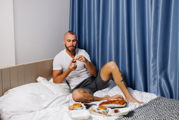 帅哥年轻人在卧室的床上吃快餐披萨盒子快餐