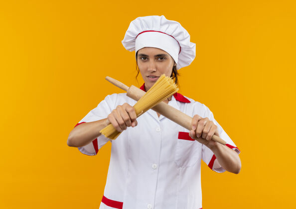 厨师年轻的女厨师穿着厨师制服 拿着擀面杖在隔离的黄色墙壁上拿着和穿过意大利面 还有复制空间看意大利面拿着