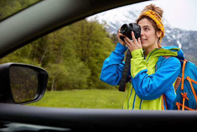 荒野专业女摄影师从车上取景用相机拍照 走在山景绿野上土地汽车背包