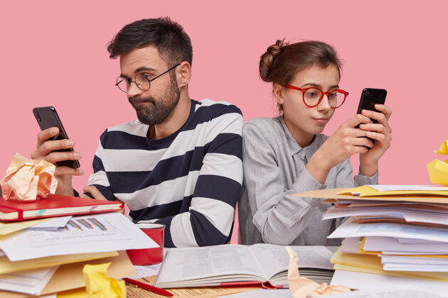 无线上瘾的年轻人坐在一起 拿着手机 上网 下班后休息 戴眼镜阅读团队合作年轻人