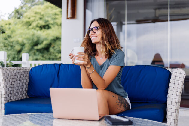 技术快乐的白种女人在家里用笔记本电脑做远程工作舒服的地方喝茶室内房子在线