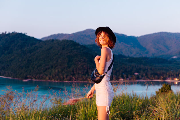 户外穿着夏装的年轻白种女人的浪漫肖像 在山上的公园里享受放松 美丽的热带海景 度假的女人 在泰国旅游日落时的快乐女人甜蜜度假耳环