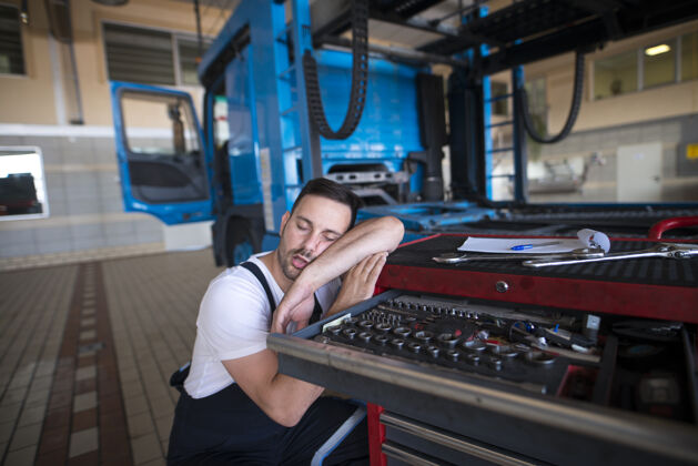 懒惰精疲力尽的汽车修理工在车间睡着了男性工作午睡