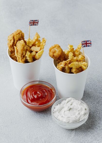 番茄酱高角度的鱼和薯条在纸杯与英国国旗和酱汁菜肴伟大鱼