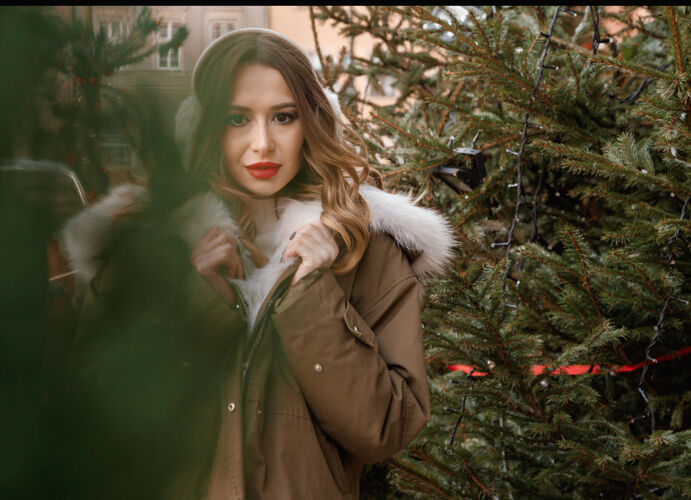无忧无虑穿着针织毛衣和蓬松耳机的白人女士户外写真年轻美丽快乐的微笑女孩穿着皮草外套在装饰圣诞树附近波兰脸黑发自然