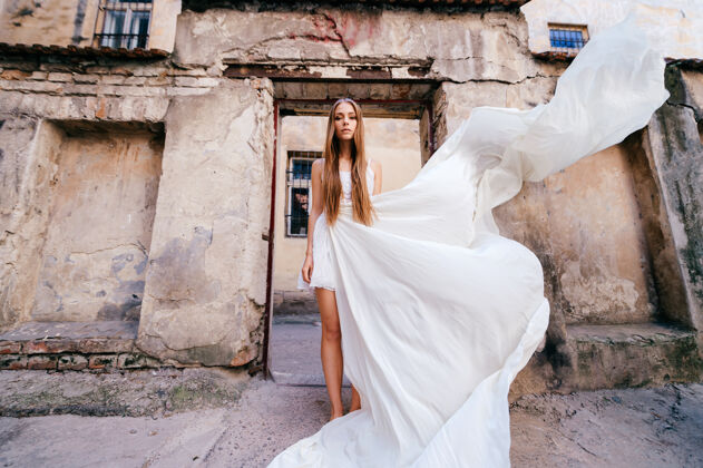 飞行服装年轻优雅的女孩 穿着白色长裙 在古老的石头建筑上摆姿势石头优雅女人