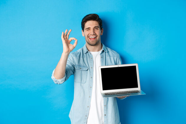 英俊年轻人展示笔记本电脑屏幕和OK标志肖像设备卓越