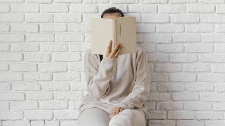 信息中等身材的女人用书遮住脸年轻女性阅读