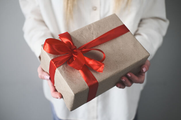 红蝴蝶结一个女人的手拿着一个带有红色缎带蝴蝶结的特写礼品盒礼物牛皮纸生日