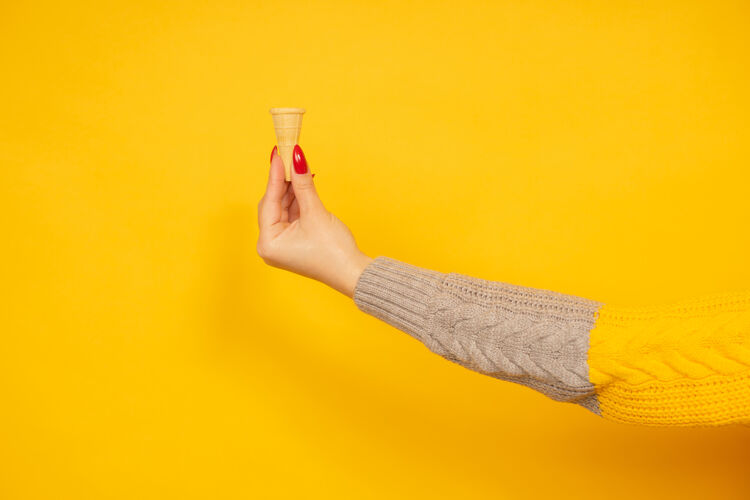 花式女人手里拿着黄色背景上孤立的小空脆冰淇淋筒毛衣吃香草